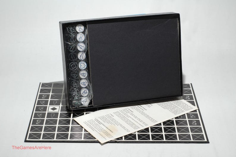 May include: A black box game with a black and white game board, a set of white and black game pieces, and a set of instructions. The game board is made of a thick cardboard and has a grid pattern. The game pieces are made of plastic and have different shapes and sizes. The instructions are printed on a sheet of paper.