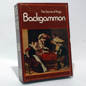 May include: A vintage game box for Backgammon, The Game of Kings. The box features a painting of people playing the game around a table with a red and gold patterned cloth.