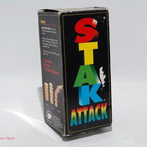 May include: A black box game called "Stack Attack" with colorful letters spelling out the name. The box shows a picture of the game in progress with wooden blocks stacked in a tower.