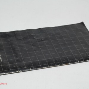 May include: A black, rectangular game manual with a grid pattern and white text. The manual is slightly crumpled and lies on a white surface. Text includes the Sega of America address.