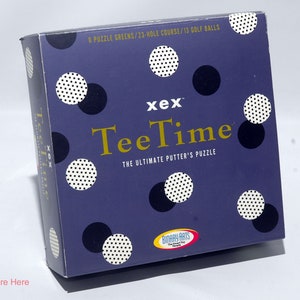 May include: A purple box with white polka dots and the text "xex TeeTime The Ultimate Putter's Puzzle" on the front. The box is for a golf-themed puzzle game.