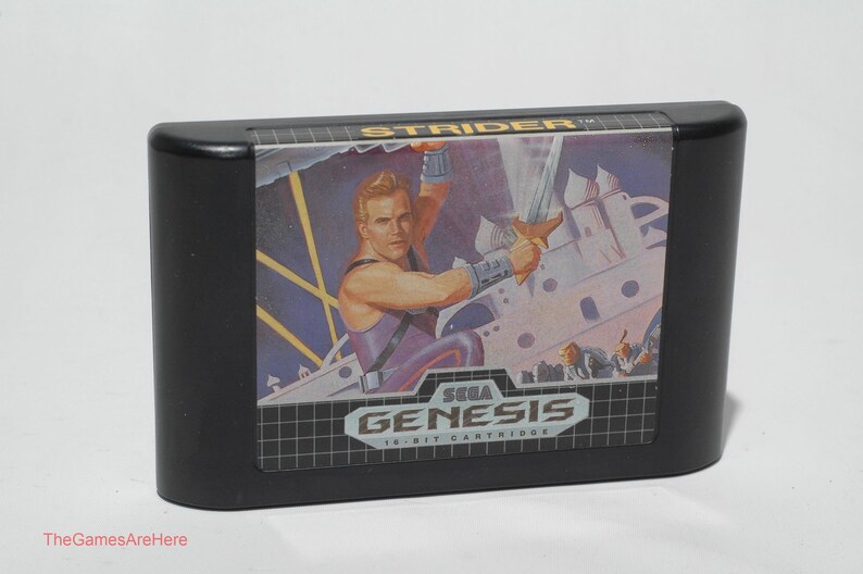 May include: Black Sega Genesis 16-bit cartridge for the game Strider. The label features a muscular man with a sword, set against a futuristic backdrop. The Sega Genesis logo is prominently displayed.