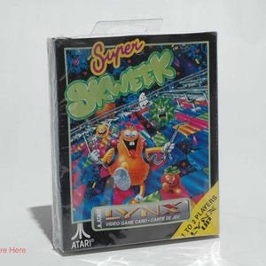 May include: A sealed Atari Lynx video game cartridge for "Super Skweek." The box features colorful cartoon characters and the game's title in a green, stylized font. The game is for 1 to 2 players.