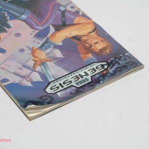 May include: A Sega Genesis 16-bit cartridge game box. The box art features a muscular man holding a sword, with a futuristic background. The Sega Genesis logo is prominently displayed. The box is on a white surface.