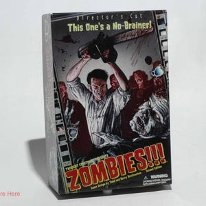 May include: A board game box titled "ZOMBIES!!!" features a graphic of a man wielding a chainsaw against zombies. The box reads "Director's Cut, This One's a No-Brainer!" and "Second Edition". The game is by Todd and Barry Sevestein.