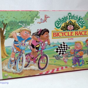 May include: A Cabbage Patch Kids Bicycle Race board game box with colorful illustrations of children riding bikes. The box features the game title "Cabbage Patch Kids Bicycle Race" and the text "Ages 4 and Up".