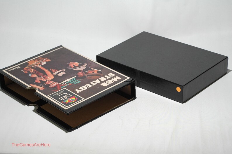 May include: A black box with a game board inside. The game board is titled "Mob Strategy" and features a colorful illustration of people playing a game. The box is open and the game board is visible.