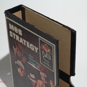 May include: A black and brown cardboard box with a game board inside. The game board is titled "Mob Strategy: The Takeover Game!" and features a colorful logo for "NB Entertainment".
