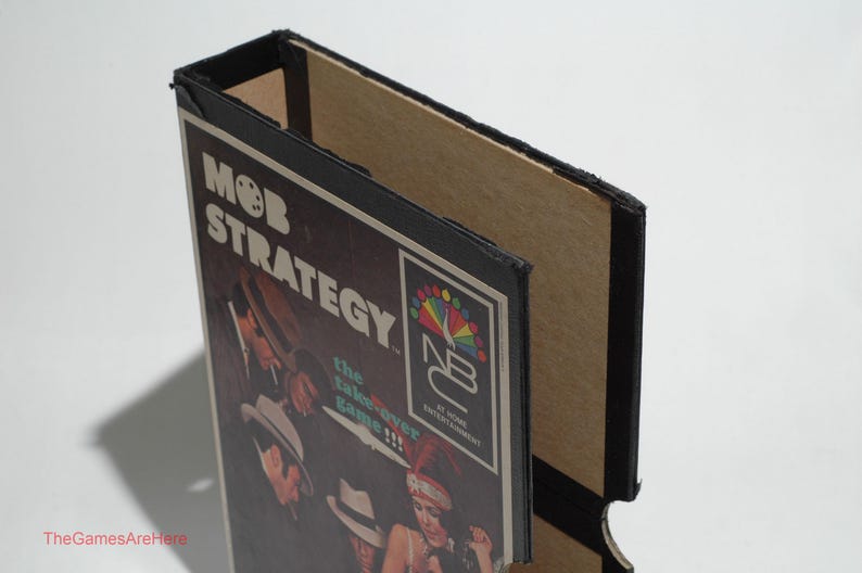 May include: A black and brown cardboard box with a game board inside. The game board is titled "Mob Strategy: The Takeover Game!" and features a colorful logo for "NB Entertainment".