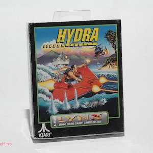 May include: A black and white Atari Lynx game cartridge with a red, white, and blue Hydra logo. The game cartridge is in a clear plastic case. The game cartridge is for the Atari Lynx handheld video game console.