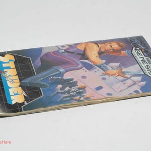 May include: Strider instruction manual for the Sega Genesis. The cover features a muscular character in a purple and blue outfit, with a futuristic cityscape background. The title "Strider" is in large, bold letters.