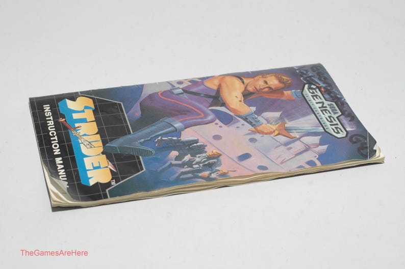May include: Strider instruction manual for the Sega Genesis. The cover features a muscular character in a purple and blue outfit, with a futuristic cityscape background. The title "Strider" is in large, bold letters.