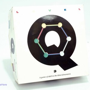 May include: A white box with the word "LEVEL" printed in red, blue, and green letters. The box features a black letter "Q" with a colorful geometric design inside. The text "A game of skill in the third dimension." is printed below the "Q".