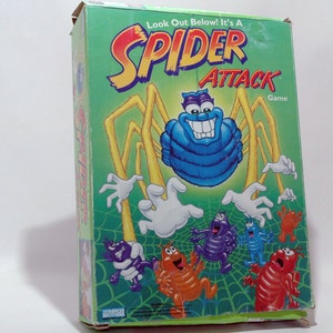 May include: A green box with a cartoon spider on the front. The spider is blue and has a big smile. The box says "Look Out Below! It's A Spider Attack Game".