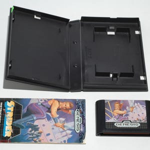 May include: An open black video game case, instruction manual, and game cartridge for the Sega Genesis game, Strider. The instruction manual features a character in purple and blue. The game cartridge is black with a colorful label.