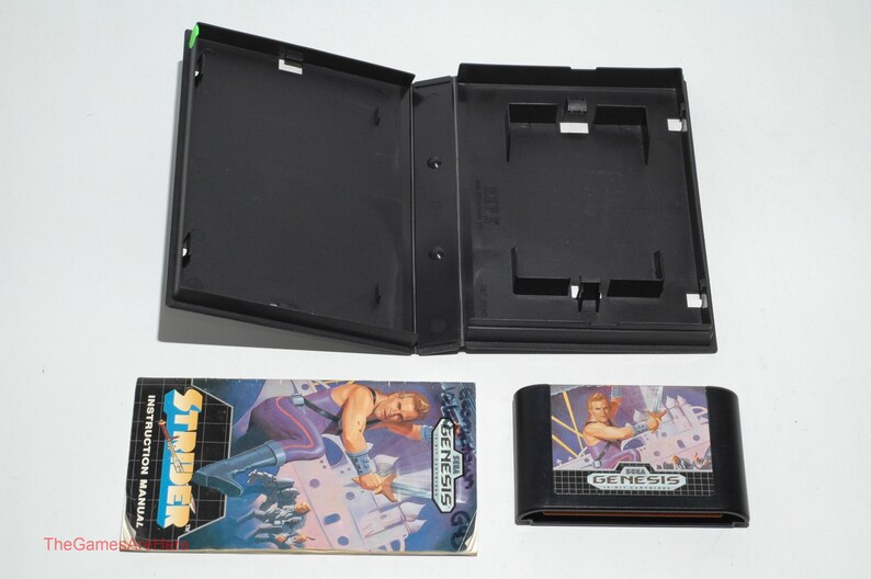 May include: An open black video game case, instruction manual, and game cartridge for the Sega Genesis game, Strider. The instruction manual features a character in purple and blue. The game cartridge is black with a colorful label.