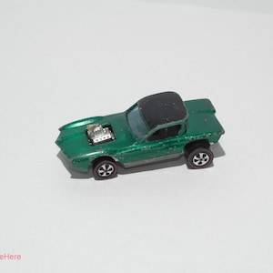 May include: A vintage green toy car with a black roof and silver engine detail. The car has black wheels with silver rims. The car is a classic toy car.