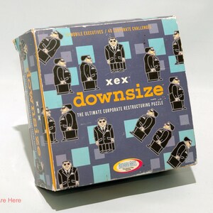 May include: A blue box with the text "xex downsize" and "THE ULTIMATE CORPORATE RESTRUCTURING PUZZLE" on the front. The box is decorated with a pattern of black and white stick figures wearing suits.