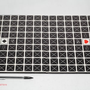 May include: A black and white grid game board with a red heart in the center. The board is made of cardboard and has a white border. The game board is folded in half.