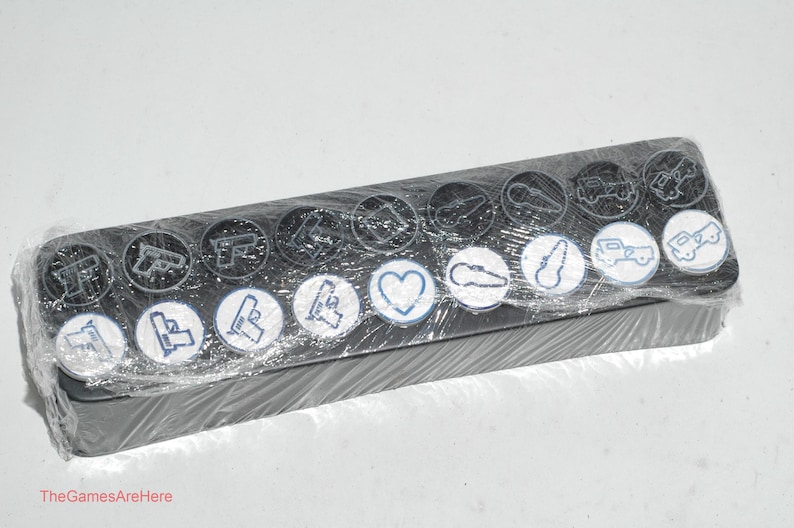May include: A black plastic case with a clear plastic cover containing 14 round black and white stickers with various symbols and designs. The symbols include a gun, a heart, a car, and a key.