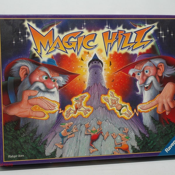 May include: A purple box with a colorful illustration of two wizards with white beards and red hats, casting magic on a mountain with a tower on top. The box says "Magic Hill" in large, bold letters. The box is from Ravensburger.