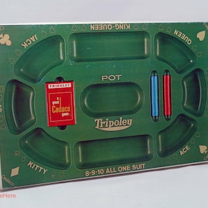 May include: A green Tripoley game board featuring molded compartments for cards and chips. The board includes text labels such as POT, KITTY, JACK, QUEEN, KING, ACE, and 8-9-10 ALL ONE SUIT. A red Tripoley card box and two cylindrical game pieces in blue and red are present.