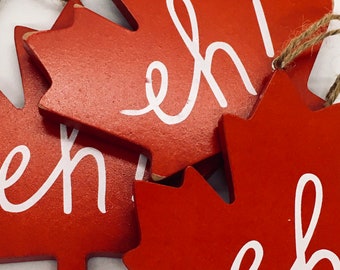 Könnte beinhalten: Drei rote Holz-Ahornblattornamente mit dem Wort "eh" in weiß auf jedem.