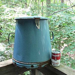 May include: A large, blue, enamelware pot with a lid and two handles. The pot is sitting on a wooden surface next to a can of Campbell's Tomato Soup.