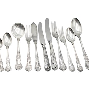 May include: A set of silver cutlery, including a knife, fork, spoon, and soup spoon. The cutlery has an ornate design with a shell motif.