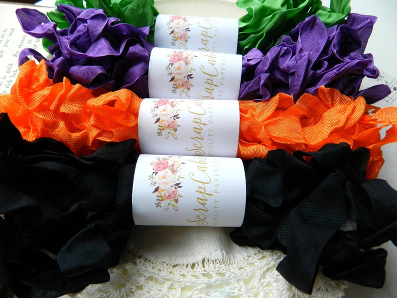 Op de afbeelding: Vier spoelen met gekrulde lint in zwart, oranje, paars en groen. De spoelen zijn gelabeld "Scrap Calico Crafts Quality Papercraft"