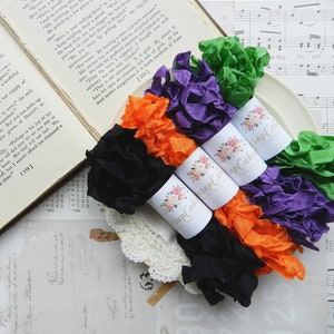 May include: Four spools of colorful ribbon in black, orange, purple, and green. The ribbon is arranged in a circle on a white plate. The spools are labeled "Wrap Cabin".
