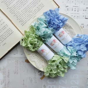 May include: Three spools of ruffled fabric ribbon in shades of light blue, green, and turquoise. Each spool is wrapped with a white label with a floral design and the text "Scrap Cabin Fabrics".