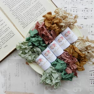 May include: Assortment of six spools of colourful ribbon in shades of green, brown, beige, and pink. Each spool is wrapped in white paper with the text "Happy Cabin" printed on it.