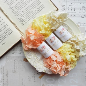 May include: Three spools of ruffled ribbon in shades of peach, yellow, and cream. Each spool is wrapped in white paper with a floral design and the text "Scrap Cabin" printed on it.