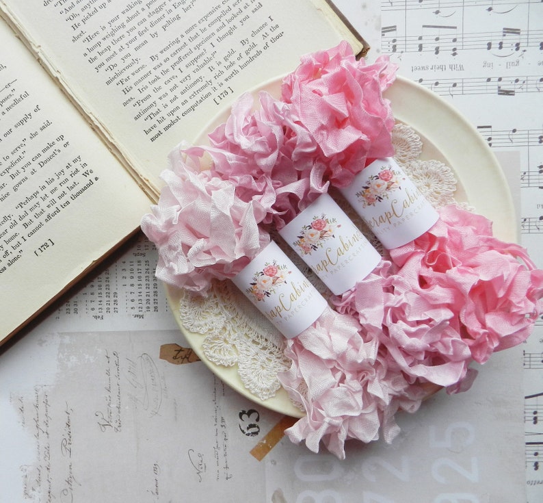 May include: Two rolls of pink and white ruffled fabric ribbon with gold labels that say "Scrap Cabin" and "Papercraft".