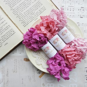May include: Three spools of pink and purple silk ribbon, each wrapped around a white label with the text "Scrap Cabin" and floral designs.
