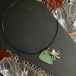 May include: A black wire choker necklace with a green sea glass charm and a silver octopus pendant.