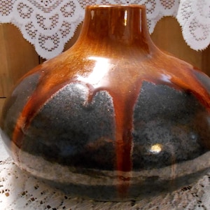 May include: A ceramic vase with a rounded body and a narrow neck. The vase has a dark gray base with brown glaze dripping down from the top, creating a unique design. The top is a solid brown color.