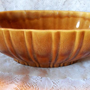 May include: A vintage, oval-shaped ceramic bowl in shades of brown and tan. The bowl has a ribbed exterior design and a glossy finish. The bowl is likely used for serving or display.