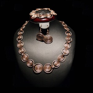May include: A copper jewelry set with a necklace, bracelet, and earrings. The necklace and bracelet are made of coiled wire, and the earrings are circular.