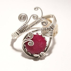 May include: A silver wire wrapped ring with a pink gemstone. The wire is twisted into a floral design.
