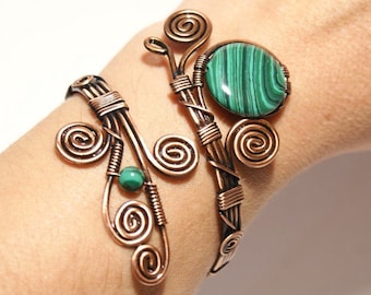 May include: Copper wire cuff bracelet with a malachite stone and green beads. The bracelet features a spiral design and is worn on the wrist. The malachite stone is oval-shaped with green and black stripes.