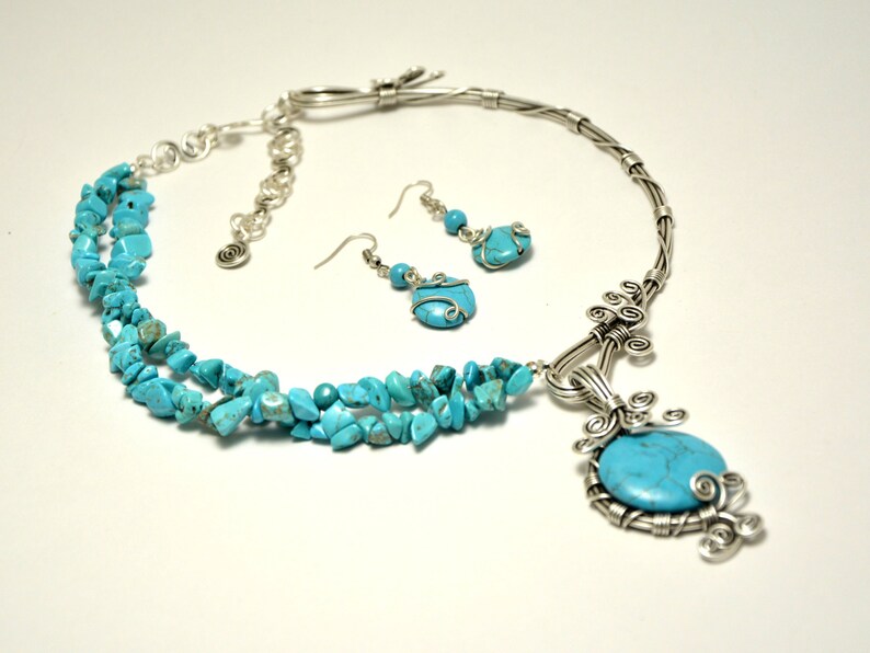 May include: A turquoise gemstone necklace and earrings set with a silver wire wrapped pendant and a silver chain. The necklace has three strands of turquoise chips.