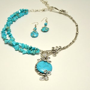 May include: A turquoise and silver necklace and earrings set. The necklace features a large turquoise stone pendant surrounded by silver wire. The earrings are simple silver hoops with a small turquoise stone.