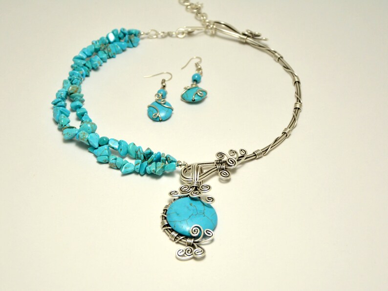 May include: A turquoise and silver necklace and earrings set. The necklace features a large turquoise stone pendant surrounded by silver wire. The earrings are simple silver hoops with a small turquoise stone.
