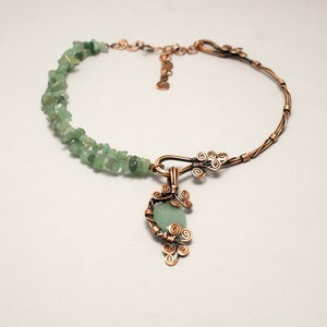 Peut inclure: Un collier en fil de cuivre avec un pendentif en pierre verte. Le collier est fait d'un fil de cuivre torsad&eacute; et a une rang&eacute;e de pierres vertes le long du dos. Le pendentif est une pierre verte envelopp&eacute;e de fil de cuivre avec un motif en fil de cuivre.