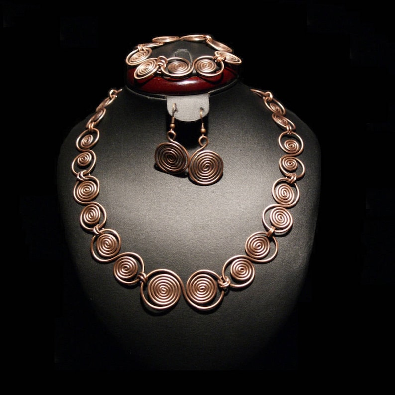May include: A copper jewelry set with a necklace, bracelet, and earrings. The necklace and bracelet are made of coiled wire, and the earrings are circular.