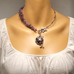 May include: A copper wire necklace with a large amethyst pendant. The pendant is wrapped in copper wire and has a delicate, leafy design. The necklace is accented with a strand of amethyst chips.