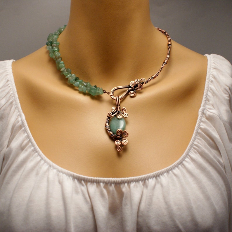 Peut inclure: Un collier en fil de cuivre avec un pendentif en pierre verte. Le collier est fait de fil de cuivre torsad&eacute; et fa&ccedil;onn&eacute; en un motif d&eacute;licat. Le pendentif est une pierre verte sertie dans un cadre en fil de cuivre. Le collier est un bijou magnifique et unique.