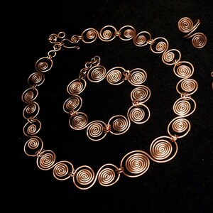 May include: A set of copper wire jewelry featuring a necklace, bracelet, and ring. Each piece is made of interconnected spiral shapes.